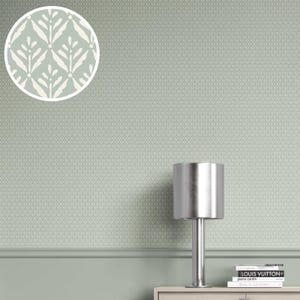 May include: A sage green wall with a repeating pattern of white leaf-like shapes. A silver lamp sits on a light-colored cabinet, with books stacked below. The wall has a decorative trim and a darker green section at the bottom.