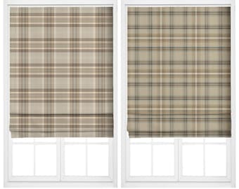 May include: Two rectangular roman shades featuring a plaid pattern. The left shade is labeled Ground Ginger with tan and brown tones. The right shade is labeled Arid Charm with beige, grey, and brown lines. Both shades are mounted on white windows.