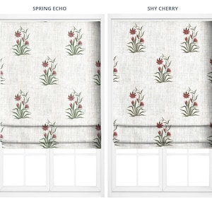 May include: Two white window shades with floral patterns. The patterns feature red flowers and green leaves on a white background. The shades are folded up at the bottom, revealing the window frames. The text "SPRING ECHO" and "SHY CHERRY" are at the top.