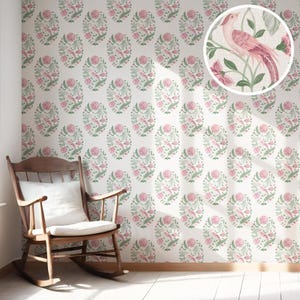 Può includere: Carta da parati con un motivo ripetuto di uccelli rosa, fiori e foglie verdi su sfondo bianco. In primo piano una sedia a dondolo in legno con un cuscino bianco. La carta da parati ha un tema floreale vintage.