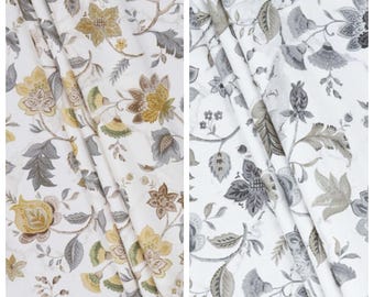 Könnte beinhalten: Zwei Stoffmuster mit floralen Mustern. Das linke Muster, mit der Bezeichnung "TUNISIA", zeigt einen weißen Hintergrund mit gelben, braunen und grauen floralen Designs. Das rechte Muster, mit der Bezeichnung "STORM VEIL", hat einen weißen Hintergrund mit grauen floralen Mustern.