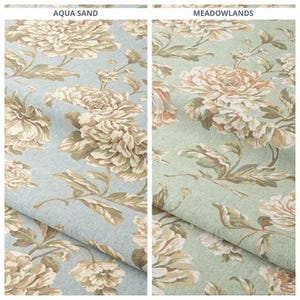 May include: Two fabric samples with floral patterns. The left sample is labeled "AQUA SAND" and features large beige and cream-colored flowers on a light blue background. The right sample, labeled "MEADOWLANDS", has similar flowers on a green background.