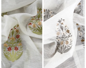 May include: White fabric with embroidered floral designs in shades of red, green, and gold. The fabric is draped, showcasing the intricate embroidery. The word "MAHZUN" is at the top left, and "DEMIR" is at the top right.