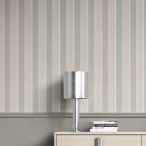 May include: A silver table lamp with a cylindrical shade sits on a light-coloured wooden cabinet. The background features vertical stripes in shades of grey and white. Books with the titles "LOUIS VUITTON" and "pierre cardin" are stacked on the cabinet.