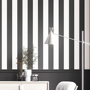 May include: A room with black and white striped wallpaper. A silver lamp with a cone-shaped shade extends from the right. A white cabinet holds a vase of dried flowers, a glass vase, and a decorative jar.