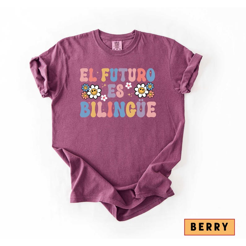 Pu&ograve; includere: T-shirt color bacca con la scritta "EL FUTURO ES BILINGUE" in lettere colorate in stile retr&ograve;. Il design include grafiche di margherite. La maglietta &egrave; di uno stile casual e confortevole.
