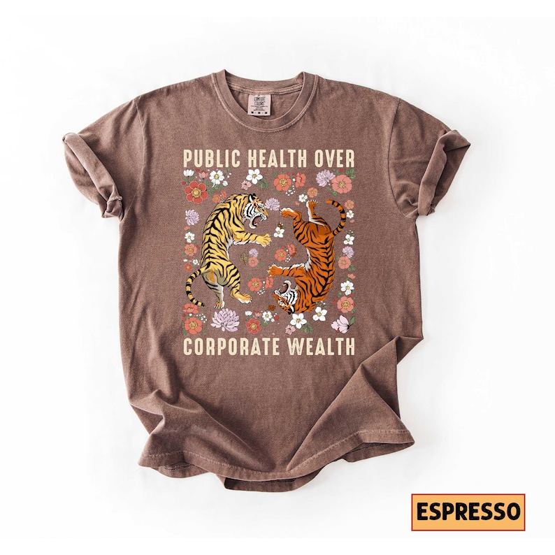 May include: Espresso-colored t-shirt with the text "PUBLIC HEALTH OVER CORPORATE WEALTH." The shirt features a graphic of two tigers surrounded by flowers. One tiger is yellow and black, the other is orange and black.