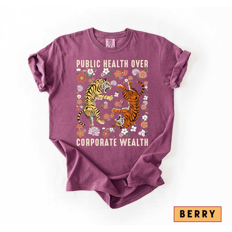 May include: Berry-colored t-shirt with the text "PUBLIC HEALTH OVER CORPORATE WEALTH." The shirt features a graphic of two tigers surrounded by flowers. One tiger is yellow and black, the other is orange and black.