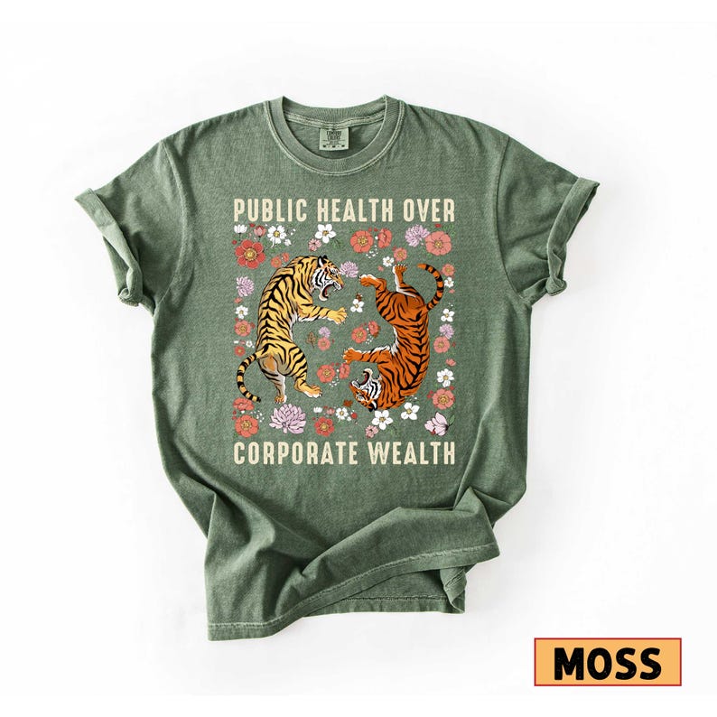May include: Moss green t-shirt with the text "PUBLIC HEALTH OVER CORPORATE WEALTH." The shirt features a graphic of two tigers surrounded by flowers. One tiger is yellow and black, the other is orange and black.