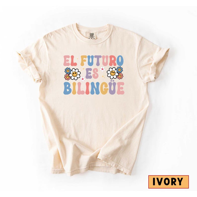 Pu&ograve; includere: T-shirt color avorio con la scritta "EL FUTURO ES BILINGUE" in spagnolo, in lettere colorate in stile retr&ograve;. Il design include grafiche floreali. La maglietta &egrave; realizzata in materiale morbido.