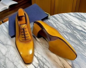 May include: A pair of yellow leather lace-up shoes with a pointed toe. The shoes have a brown leather sole and a brown leather heel.