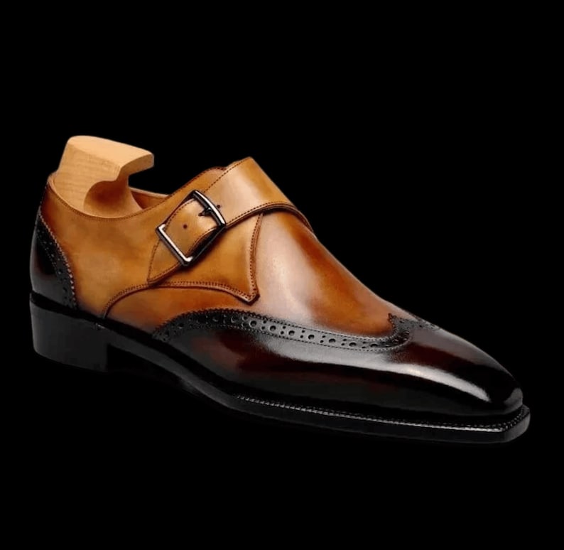 May include: A brown and black leather dress shoe with a single buckle strap and wingtip design.