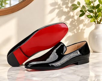 May include: A pair of black patent leather loafers with a high-gloss finish. One shoe is positioned to display the smooth black upper, while the other is angled to reveal the vibrant, solid red sole and a low, stacked black heel.