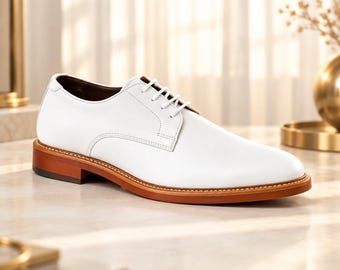 May include: A white leather oxford shoe featuring a smooth upper, a rounded toe, and white laces. The shoe is constructed with a distinct brown wooden-toned sole and a low heel, showcasing visible stitching along the welt of the shoe base.