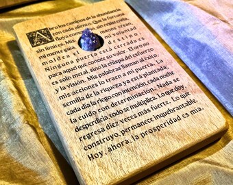 May include: A wooden box with a purple crystal embedded in the front. The box has a message engraved on it that reads: "Bro los caminos de la abundancia con cada aliento. Que la fortuna fluya como rio, sin resistencia, sin limites. Mis manos crean, mi voluntad moldea el destino. Ninguna puerta esta cerrada es para aquel que conoce su valor. El oro no es solo metal, sino la chispa del esfuerzo y la vision. Mis palabras llaman al exito, mis acciones lo traen a mi puerta. La semilla de la riqueza ya esta plantada; cada dia la riego con intencion, cada noche la cuido con determinacion. Nada se desperdicia, todo se multiplica. Lo que doy, regresa diez veces mas fuerte. Lo que construyo, permanece inquebrantable. Hoy, ahora, la prosperidad es mia."