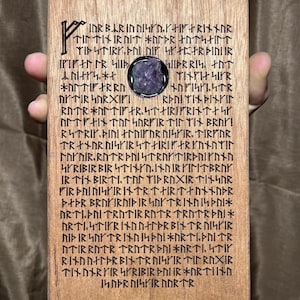 Könnte beinhalten: Rechteckige Holztafel mit eingeritzten Runen und einem Amethyststein. Die Runen sind dunkelbraun, und das Holz hat eine natürliche Maserung. Die Tafel wird von einer Person gehalten. Ungefähre Größe: 15 cm x 10 cm.