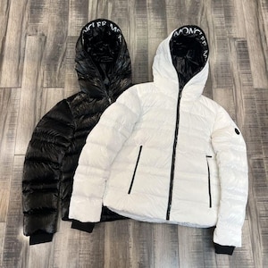 May include: Two hooded puffer jackets, one black and one white, are displayed. The jackets have a shiny, quilted texture, black zippers, and the brand name printed on the hood lining. The jackets are on a wooden surface.