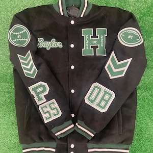 May include: Black varsity jacket with green and white accents. Features patches with a baseball, football, chevrons, and the text "Baylor", "H CLASS OF 2026", "PASS", and "QB".