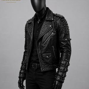 Könnte beinhalten: Schwarze Lederjacke mit silbernen Nieten und Spikes auf den Schultern und Ärmeln. Die Jacke hat einen klassischen Biker-Stil mit Reverskragen, asymmetrischem Reißverschluss und mehreren Taschen. Die Ärmel haben Schnallendetails. Der Markenname "AURAANDHIDE" ist sichtbar.