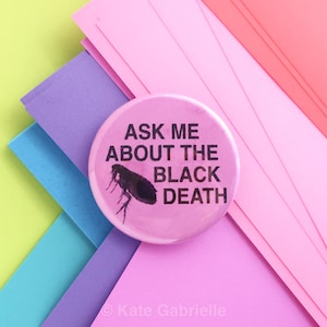 Puede incluir: Un botón redondo rosa con el texto "ASK ME ABOUT THE BLACK DEATH" y una ilustración negra de una pulga. El botón está sobre un fondo de papel pastel en capas de color rosa, morado y azul.