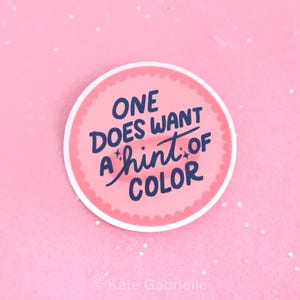May include: A round sticker with a pink background and a white border. The sticker features the text "ONE DOES WANT A hint of COLOR" in navy blue script. The sticker is on a pink background with glitter.