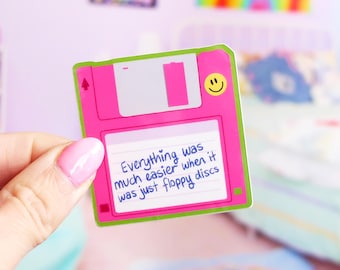 May include: A pink floppy disk sticker with a green border and a smiley face. The sticker has the text "Everything was much easier when it was just floppy discs" written on it.