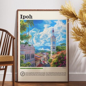 Può includere: Una stampa artistica incorniciata con una vivace illustrazione di Ipoh, Malesia. L'opera d'arte mostra edifici colorati, una torre dell'orologio e una vegetazione lussureggiante sotto un cielo blu brillante con nuvole soffici. La parola "Ipoh" è in alto.