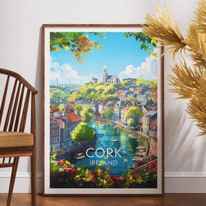 May include: A framed art print featuring a scenic view of Cork, Ireland. The artwork depicts a river flowing through a town with colorful buildings, a church on a hill, and the text "CORK IRELAND". The print has a wooden frame.