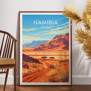 Könnte beinhalten: Gerahmter Kunstdruck mit einer stilisierten Landschaft Namibias, Afrika. Das Kunstwerk zeigt eine lebendige Wüstenlandschaft mit rot-orangen Dünen, einer unbefestigten Straße und einem blauen Himmel mit Wolken. Das Wort "NAMIBIA" ist oben aufgedruckt.