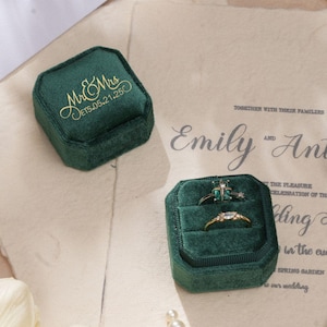 May include: A wedding-themed image with a dark green velvet ring box inscribed with "Mr & Mrs" and a date in gold. Another ring box contains two rings. A wedding invitation, a quill pen, and pearls are also visible.