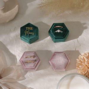 Puede incluir: Cuatro joyeros hexagonales de terciopelo en tonos verdes y rosas. Dos joyeros est&aacute;n abiertos, mostrando anillos con diamantes y piedras preciosas. Un joyero verde tiene el texto dorado "The Moons". Los joyeros est&aacute;n colocados sobre una superficie clara.