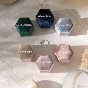 May include: A collection of hexagonal velvet ring boxes in various colors: Deep Emeralds, Winter Blue, Powder Blue, Champagne, Nude Pink, and Rose Pink. A silver ring is placed in the center. The word "COLORS" is at the top.