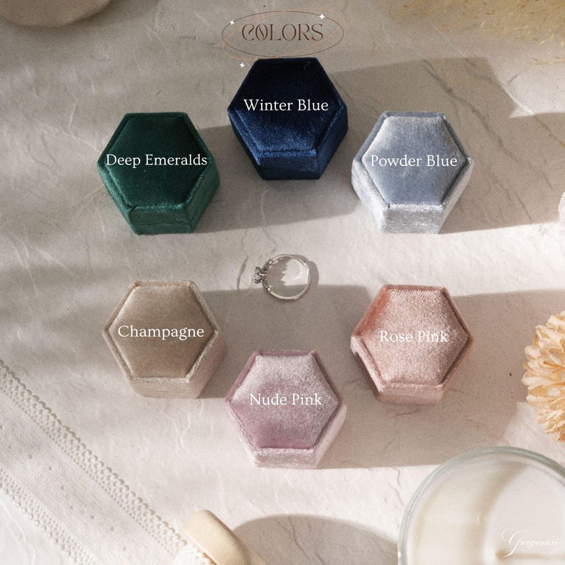 Puede incluir: Una colecci&oacute;n de joyeros hexagonales de terciopelo en varios colores: Deep Emeralds, Winter Blue, Powder Blue, Champagne, Nude Pink y Rose Pink. Un anillo de plata est&aacute; colocado en el centro. La palabra "COLORS" est&aacute; en la parte superior.