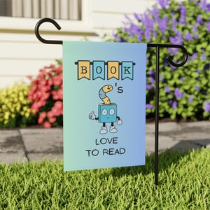 Puede incluir: Una bandera de jardín azul y verde con un personaje de libro de dibujos animados y el texto "BOOK'S LOVE TO READ".
