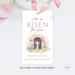 Pode incluir: Uma etiqueta branca com uma fita rosa apresenta o texto "He is Risen for you" em uma fonte de script. Abaixo está uma imagem em aquarela de Jesus em frente a um túmulo de pedra. As palavras "Happy Easter" também estão incluídas.
