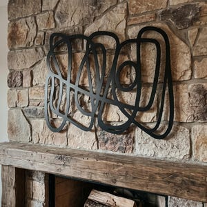 May include: A black metal wall art piece featuring a continuous, abstract line design with multiple overlapping loops and curves. The structure is composed of thin, flat metal strips arranged in a complex, interconnected pattern that creates a large, singular decorative object.