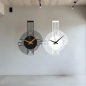 May include: Two modern wall clocks. One clock is black with gold hands, the other is white with black hands. Both clocks have a circular design with geometric shapes and a rectangular top.