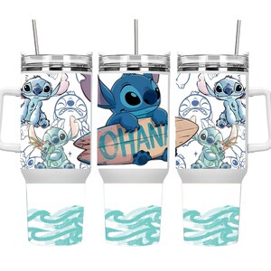 May include: White travel mug featuring a blue cartoon character holding a surfboard with the word "OHANA" on it. The mug has a handle, a silver lid, and a straw. The design includes various images of the character and a blue wave pattern.