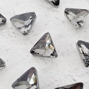 May include: A group of small, clear, triangular rhinestones with a dark gray color.