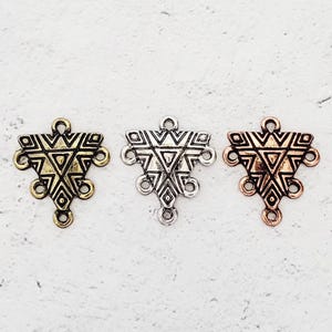May include: Three triangle-shaped metal charms with a geometric design. The charms are in silver, gold, and copper.