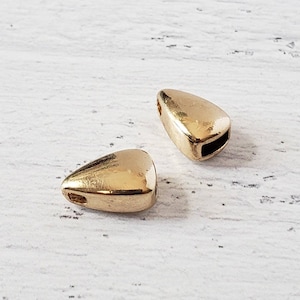 May include: Two gold-colored triangle-shaped beads with a hole in the center. The beads are on a white surface.