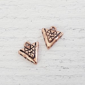 May include: Two copper-colored triangle charms with a geometric pattern. The charms have a loop at the top for attaching to jewelry or other crafts.