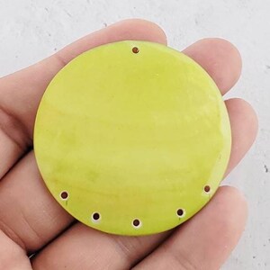 May include: A round, lime green, ceramic pendant with six holes around the edge and one hole at the top for hanging.