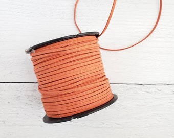 Könnte beinhalten: Eine Spule mit orangefarbenem Wildlederband, das um eine schwarze Plastikspule gewickelt ist. Das Band ist dünn und hat eine glatte, leicht strukturierte Oberfläche.