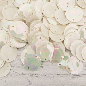 May include: A pile of white iridescent round sequins with two holes in each sequin.