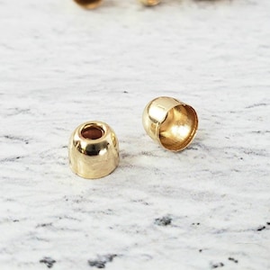 May include: Gold-colored metal end caps for cords or jewelry making. The caps are round and have a small hole in the center.