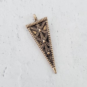 May include: A gold-toned triangle pendant with a geometric design. The pendant has a loop at the top for attaching to a chain or cord.