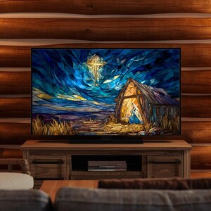 May include: A large flat-screen television displays a stained-glass style image of a nativity scene. The artwork features a star, a barn, and figures in a field, set against a blue and gold sky. The TV sits on a wooden cabinet.
