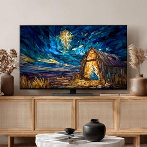 May include: A flat-screen television displays a stained-glass style image of a nativity scene. The artwork features a star, a stable, and figures in blue and gold against a dark blue sky. The TV sits on a light wood cabinet.