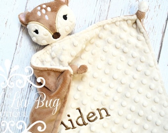 May include: A plush security blanket featuring a brown and cream-colored deer head with embroidered facial features. The blanket has a cream-colored minky fabric with a raised dot texture and the name Aiden embroidered in brown thread.
